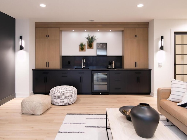 bar featuring light wood-style floors, beverage cooler, indoor wet bar, and a sink