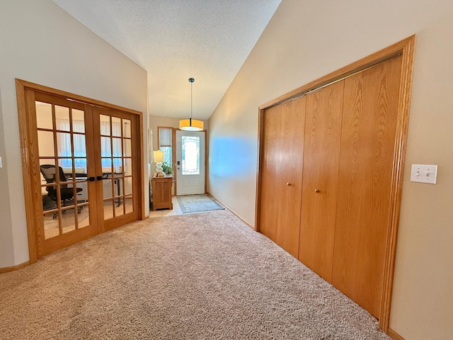 carpeted entrance foyer featuring french doors, vaulted ceiling, and a textured ceiling