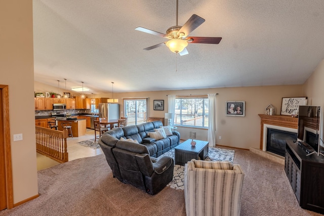 living room featuring light colored carpet, a textured ceiling, a ceiling fan, a glass covered fireplace, and baseboards