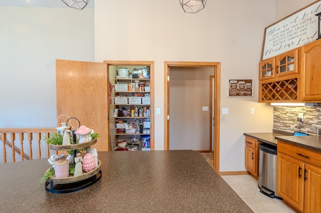 kitchen with dark countertops, backsplash, light tile patterned flooring, a high ceiling, and glass insert cabinets
