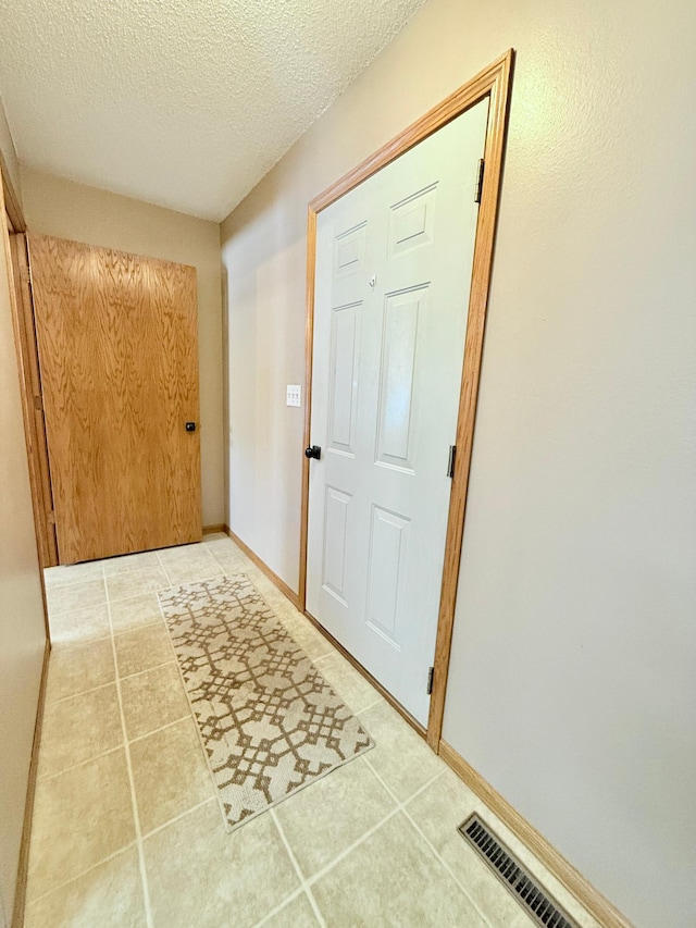 doorway to outside with tile patterned floors, a textured ceiling, and baseboards