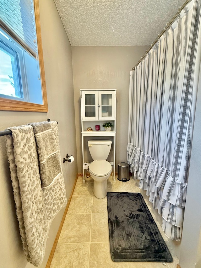 full bathroom featuring tile patterned floors, toilet, a textured ceiling, curtained shower, and baseboards