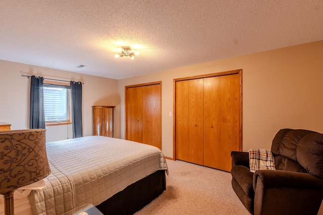 bedroom featuring light colored carpet, two closets, and a textured ceiling