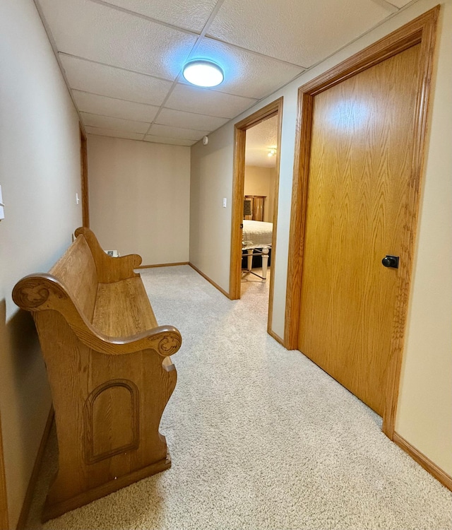 corridor featuring carpet flooring, a paneled ceiling, and baseboards