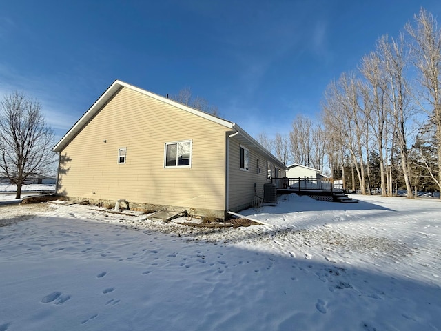 view of snowy exterior with a wooden deck and central air condition unit