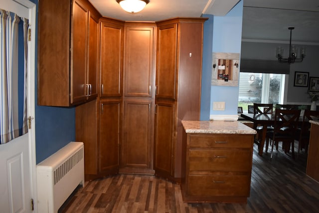 kitchen with dark hardwood / wood-style flooring, light stone counters, crown molding, radiator heating unit, and hanging light fixtures