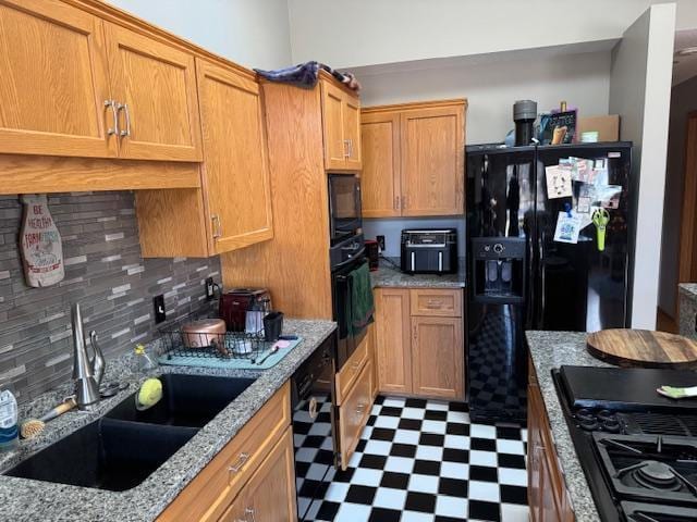 kitchen with backsplash, light stone countertops, sink, and black appliances