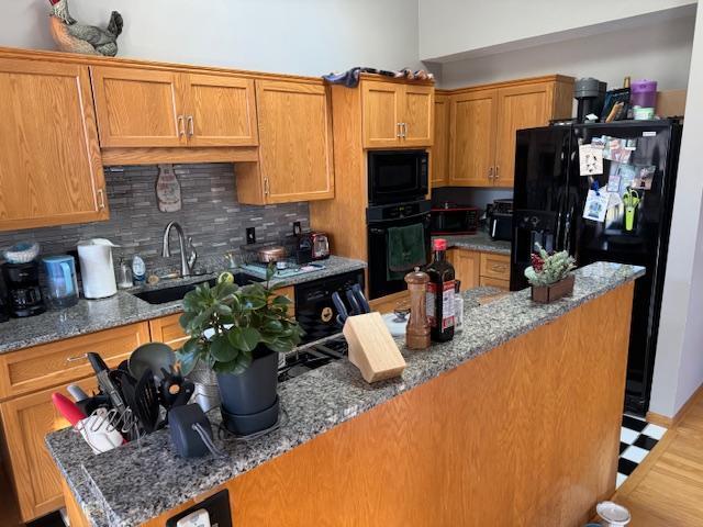 kitchen with decorative backsplash, sink, black appliances, and stone countertops