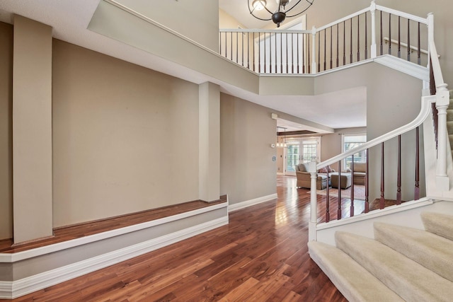 staircase with a high ceiling, hardwood / wood-style flooring, and a notable chandelier