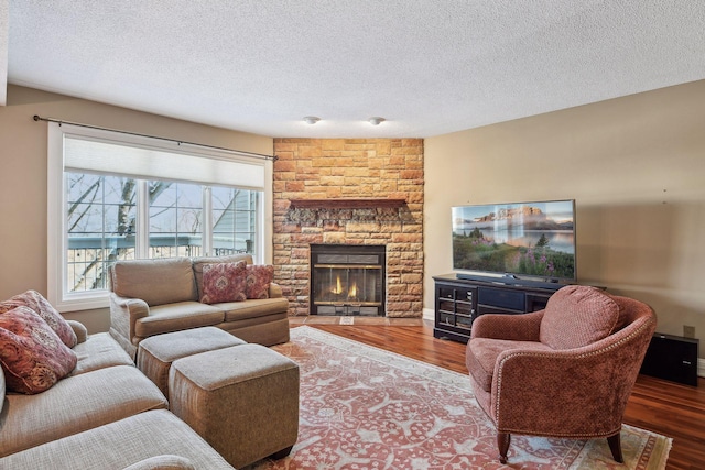 living room featuring hardwood / wood-style flooring, plenty of natural light, a textured ceiling, and a stone fireplace