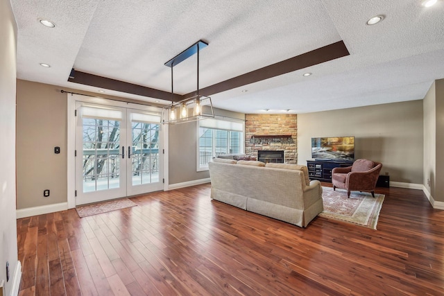 living room featuring dark wood-type flooring, a textured ceiling, a stone fireplace, and french doors