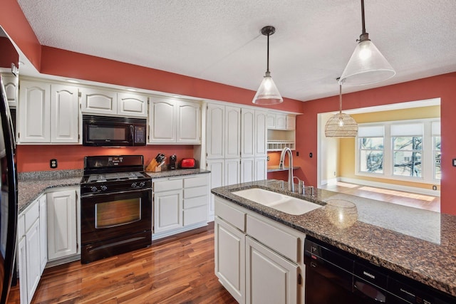 kitchen with decorative light fixtures, dark stone counters, black appliances, white cabinets, and sink