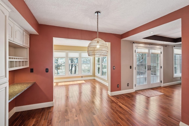 unfurnished dining area featuring dark wood-type flooring, a raised ceiling, french doors, and a healthy amount of sunlight