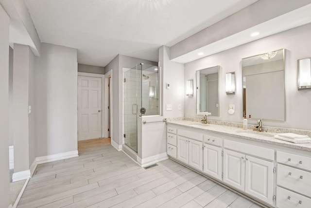 bathroom with hardwood / wood-style flooring, a textured ceiling, an enclosed shower, and vanity