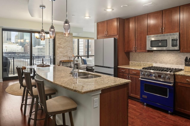 kitchen featuring a sink, freestanding refrigerator, high end range, stainless steel microwave, and a center island with sink