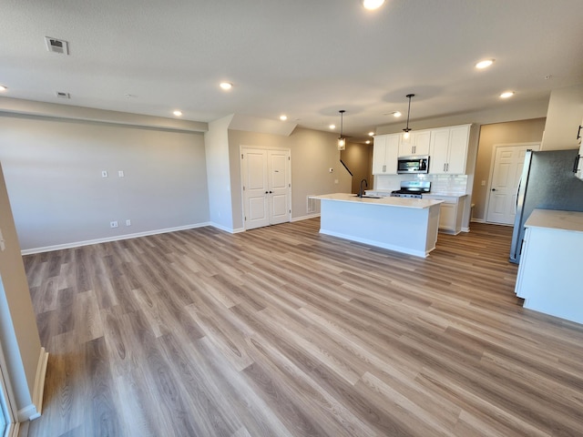 kitchen featuring a kitchen island with sink, white cabinets, hanging light fixtures, light hardwood / wood-style flooring, and appliances with stainless steel finishes