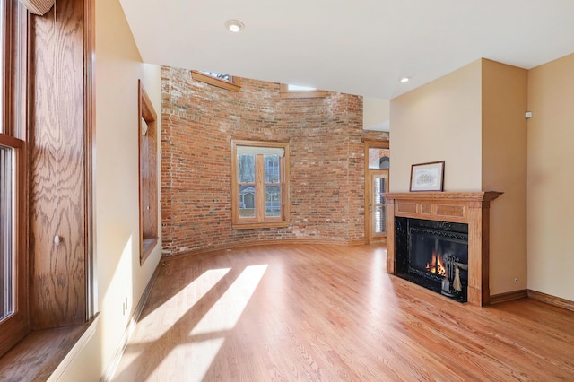 unfurnished living room featuring a fireplace, light wood-type flooring, and brick wall