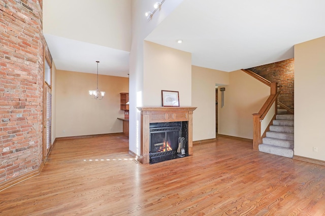 unfurnished living room with a chandelier, light wood-type flooring, and brick wall