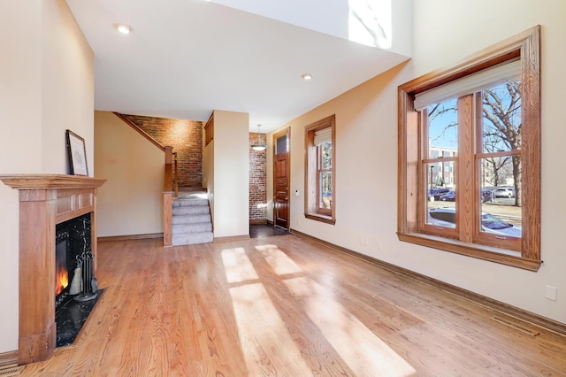 unfurnished living room with a fireplace, brick wall, and light hardwood / wood-style floors