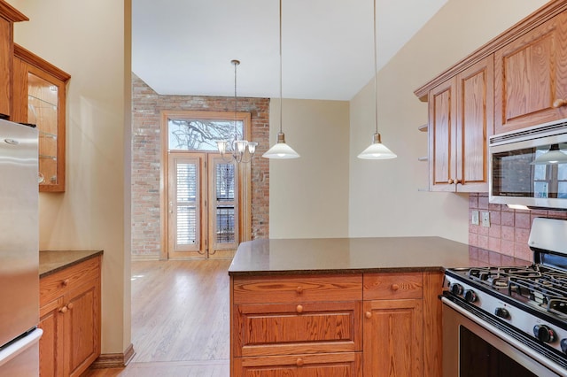 kitchen with light wood-type flooring, brick wall, stainless steel appliances, an inviting chandelier, and hanging light fixtures