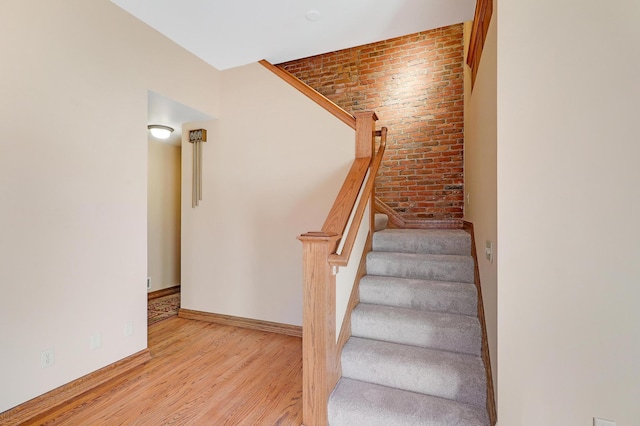 stairs with wood-type flooring and brick wall