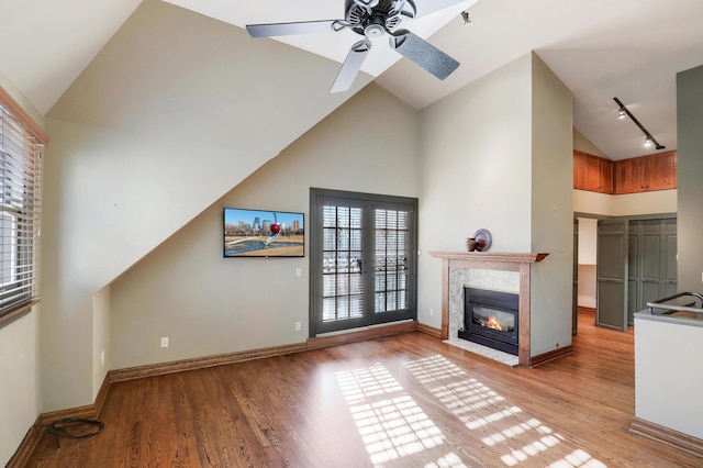 unfurnished living room with ceiling fan, rail lighting, a high end fireplace, and light hardwood / wood-style flooring