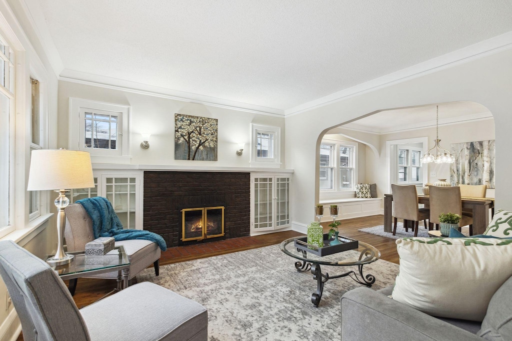 living room featuring an inviting chandelier, a brick fireplace, crown molding, and hardwood / wood-style floors