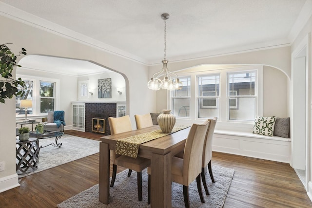 dining space with dark wood-type flooring, crown molding, and a fireplace