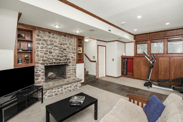 living room featuring built in shelves, a stone fireplace, and crown molding