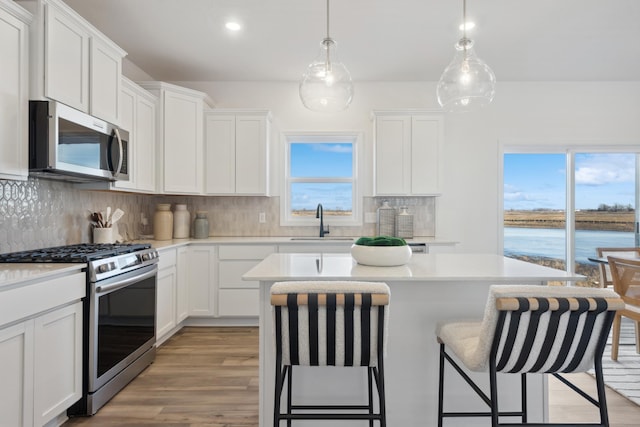 kitchen featuring sink, stainless steel appliances, a kitchen island, a water view, and white cabinets