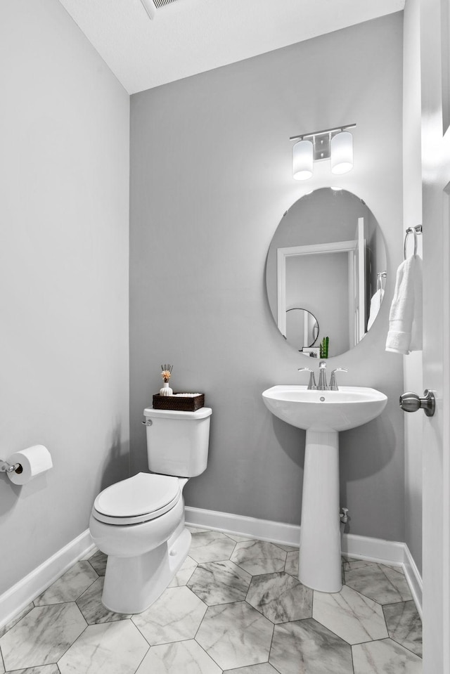 bathroom featuring marble finish floor, toilet, baseboards, and a sink