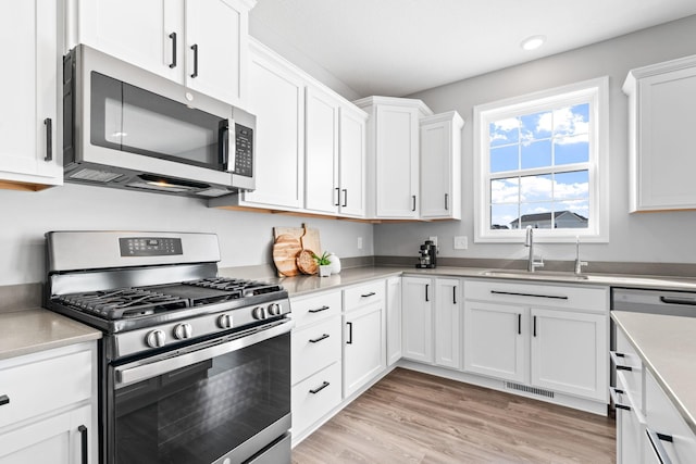 kitchen featuring a sink, light wood-style floors, appliances with stainless steel finishes, and white cabinetry