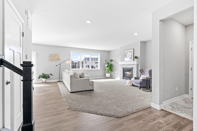 living room featuring stairway, light wood-style flooring, a stone fireplace, and baseboards