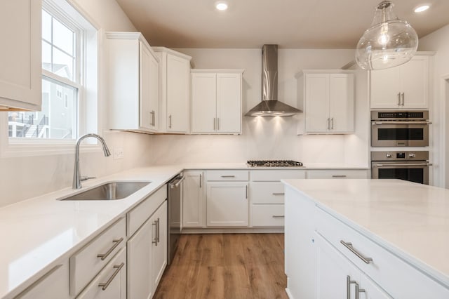 kitchen with wall chimney exhaust hood, white cabinetry, and sink