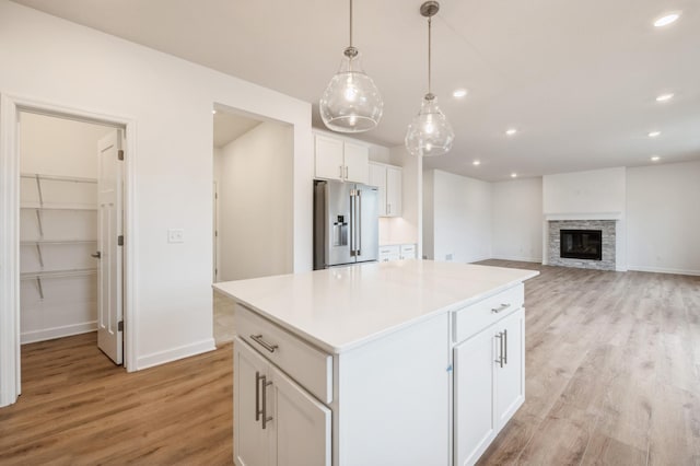 kitchen with a kitchen island, decorative light fixtures, high quality fridge, a fireplace, and white cabinets