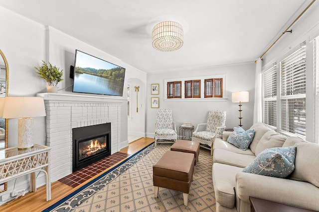 living room with arched walkways, a brick fireplace, crown molding, and wood finished floors