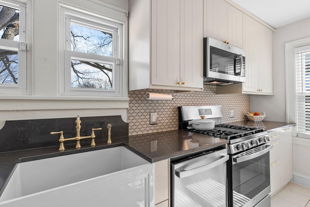 kitchen featuring dark countertops, stainless steel appliances, tasteful backsplash, and a sink