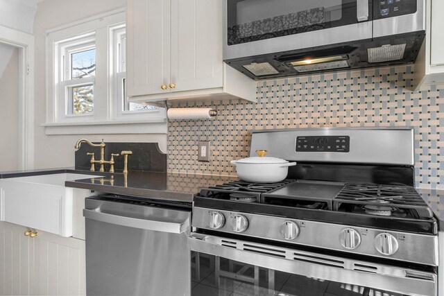 kitchen featuring a sink, white cabinets, appliances with stainless steel finishes, dark countertops, and backsplash