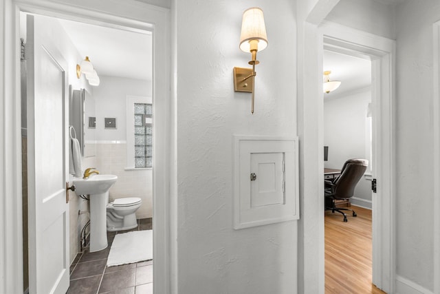 bathroom featuring toilet, wainscoting, tile patterned floors, tile walls, and a sink