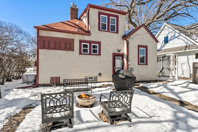 snow covered property with stucco siding and a chimney