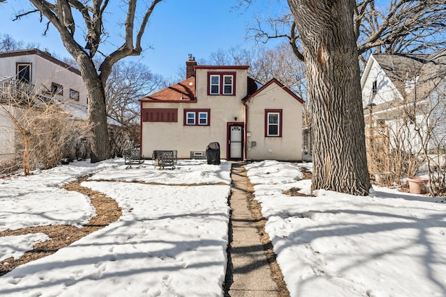 snow covered rear of property with stucco siding and a chimney