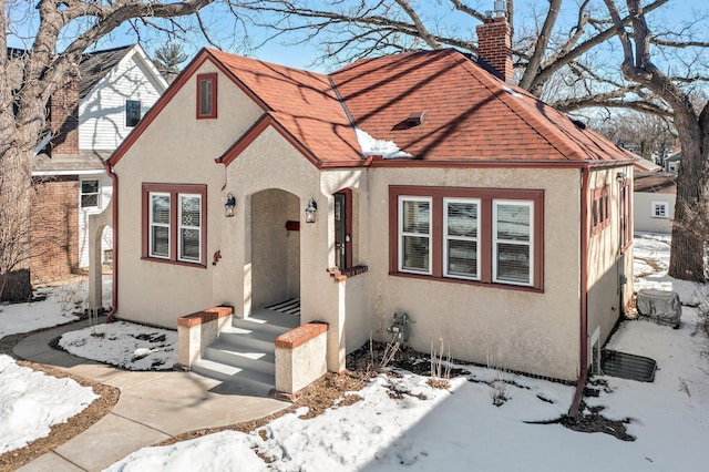 view of front of house featuring stucco siding, a chimney, and a shingled roof