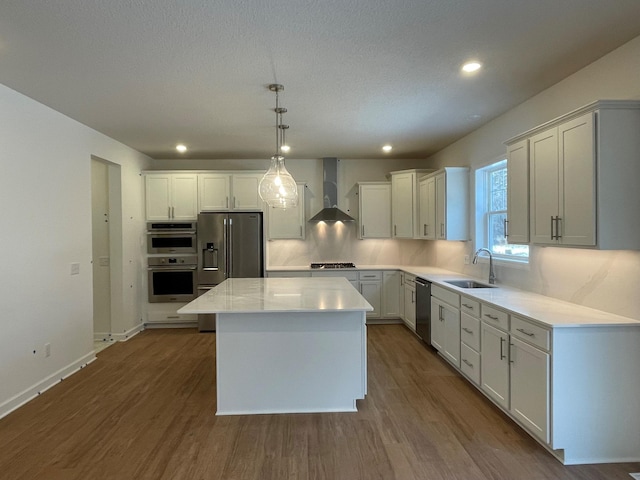 kitchen with pendant lighting, wall chimney range hood, appliances with stainless steel finishes, a kitchen island, and white cabinetry