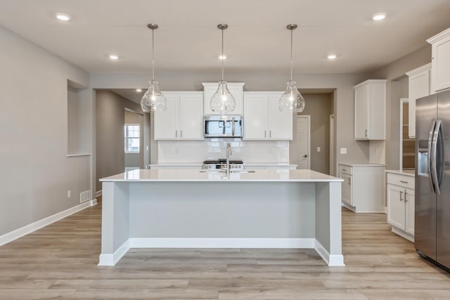 kitchen with white cabinets, a kitchen island with sink, hanging light fixtures, and appliances with stainless steel finishes