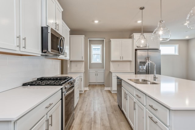 kitchen featuring sink, hanging light fixtures, stainless steel appliances, a center island with sink, and white cabinets