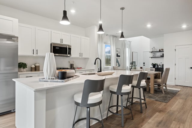 kitchen with white cabinets, appliances with stainless steel finishes, a center island with sink, and hanging light fixtures