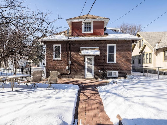 snow covered rear of property featuring brick siding and fence