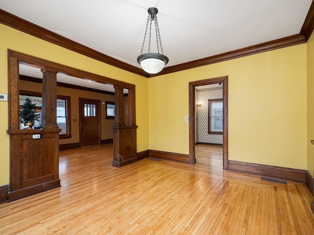 spare room featuring baseboards, crown molding, light wood finished floors, and ornate columns