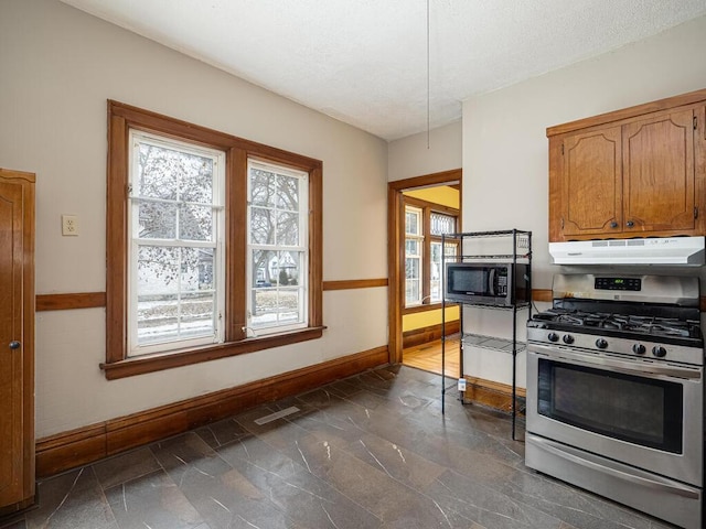 kitchen with under cabinet range hood, visible vents, baseboards, brown cabinets, and gas range