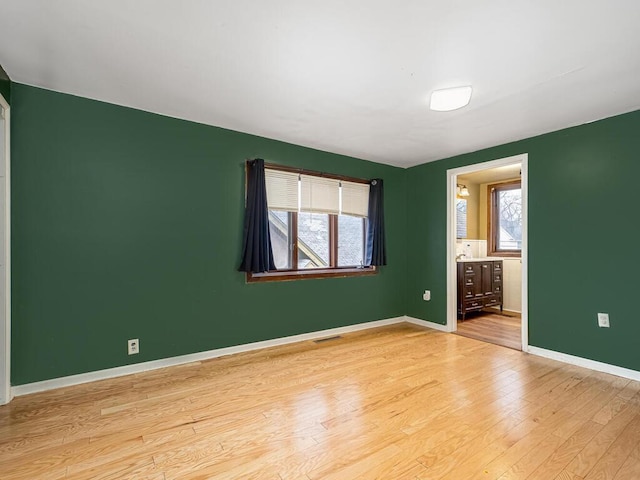 empty room featuring a wealth of natural light, visible vents, light wood-style flooring, and baseboards